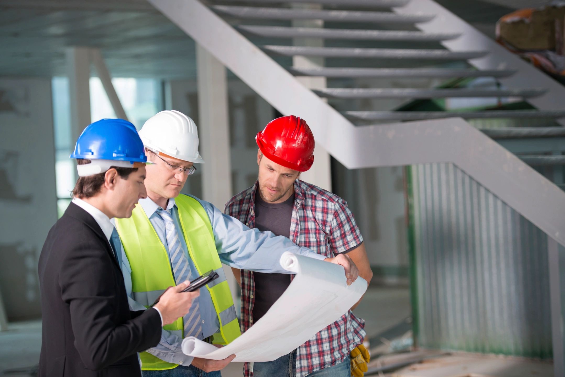 Three construction workers examining building plans indoors.